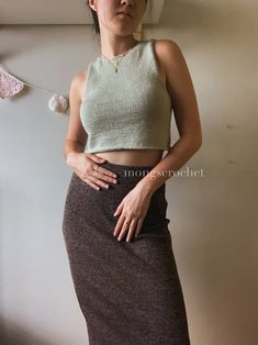 a woman standing in front of a wall with her hands on her hips wearing a skirt and crop top