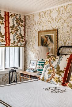 a bed sitting in a bedroom next to a window covered in wallpaper and pillows