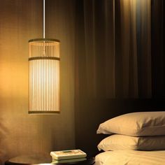 a lamp hanging over a bed next to a night stand with a book on it