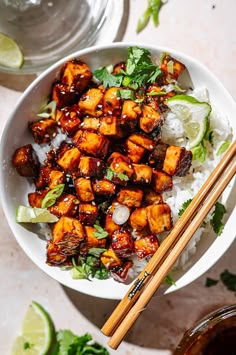 a white bowl filled with tofu and rice next to chopsticks on a table