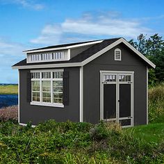 a small gray shed sitting on top of a lush green field next to a body of water