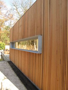 the side of a wooden building with a window on it's side and trees in the background