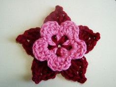 a crocheted flower is shown on a white surface with red and pink yarn