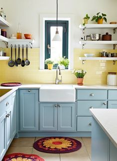 a kitchen with yellow and blue cabinets, white counter tops and rugs on the floor