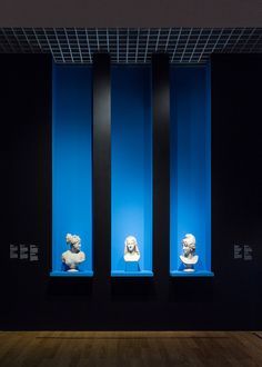 three white busturines on display in a room with black walls and blue lighting