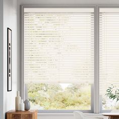 a living room with white furniture and large windows covered in blinds that look out onto the trees outside