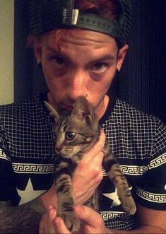 a man holding a kitten in front of his face while wearing a helmet on top of his head