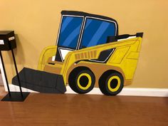 a cardboard construction vehicle sitting on top of a hard wood floor next to a wall