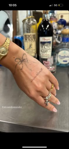 a woman's hand with tattoos on it and some bottles in the back ground