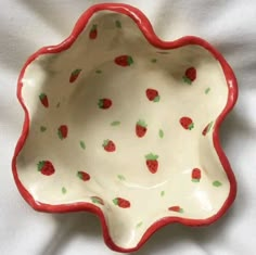 a red and white bowl with strawberries on it's rim sitting on a bed