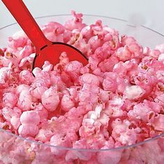 a bowl filled with pink popcorn sitting on top of a table next to a red spoon