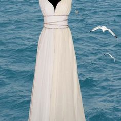 a white dress on a mannequin in the water with seagulls flying around