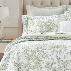 a bed with a green and white comforter on top of it next to a night stand