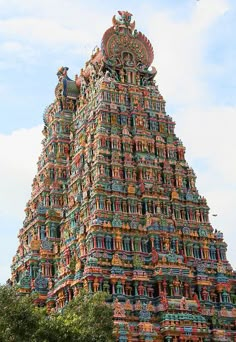 a very tall tower with many different colored sculptures on it's sides and trees in the foreground