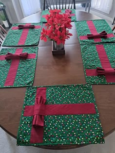 a wooden table topped with green and red placemats next to a vase filled with flowers