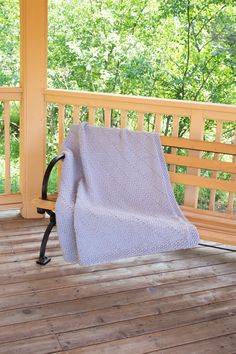 a blanket sitting on top of a wooden porch next to a bench and trees in the background