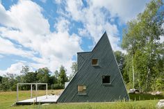 a triangular shaped house in the middle of a field with trees and grass around it