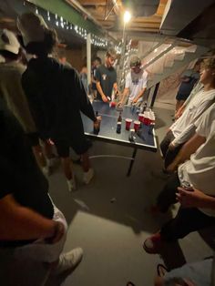 a group of people standing around a ping pong table in a room with lights on