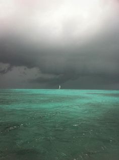 a sailboat is in the distance under a cloudy sky over the ocean with green water