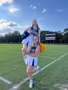 two cheerleaders pose for a photo on the field