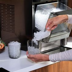 two people are filling glasses with ice in front of a toaster on a counter