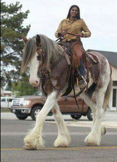 a woman riding on the back of a brown and white horse in a parking lot