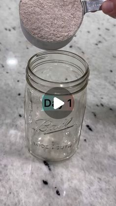 a person holding a spoon over a mason jar