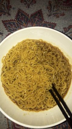 a white bowl filled with noodles and chopsticks on top of a carpeted table