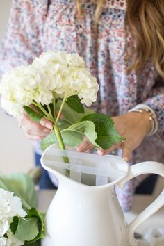 a woman arranging flowers in a white pitcher