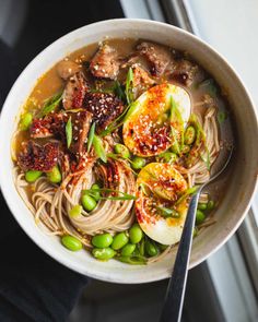 a white bowl filled with noodles, meat and veggies next to a window