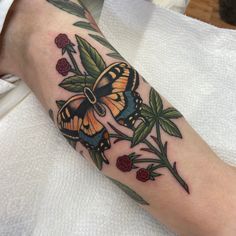 a colorful butterfly sitting on top of a plant with leaves and berries around its legs