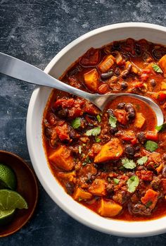 a white bowl filled with chili and tofu soup next to limes on the side