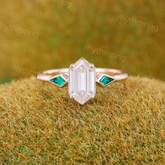 an emerald and diamond ring sitting on top of some brown grass with the background green