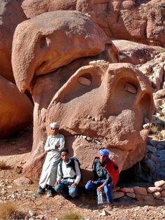 three people are sitting in front of a large rock formation with a face carved into it