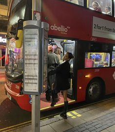 a woman getting on a double decker bus at night