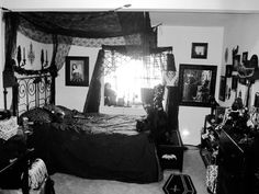 black and white photograph of a bedroom with bed, dressers, mirror and pictures on the wall