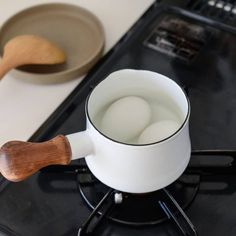 an egg in a cup on top of a stove with a wooden spoon next to it