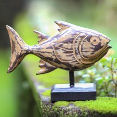 a small wooden fish statue sitting on top of a moss covered rock next to a plant