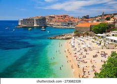 the beach is crowded with people and boats in the blue water near an old city