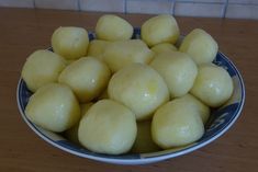 a blue and white bowl filled with potatoes on top of a wooden table next to a tile wall