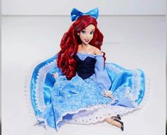 a doll with red hair and blue dress sitting on top of a white tablecloth