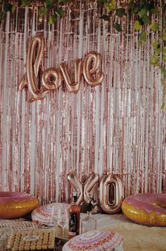 a table topped with lots of balloons and donuts next to a wall covered in streamers