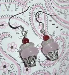 two cupcakes with frosting and red beads are hanging from silver earwires