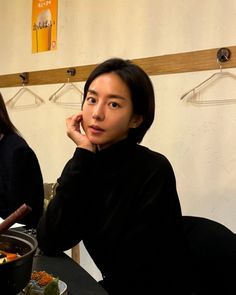 a woman sitting at a table with food in front of her and another person standing behind her