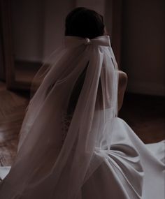 the back of a bride's veil as she sits in her wedding dress on the floor