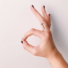 a person's hand with a cross tattoo on their thumb and the middle finger