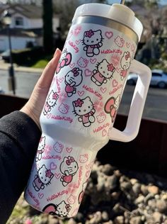 someone holding up a hello kitty travel mug in their left hand, with hearts and bows on it