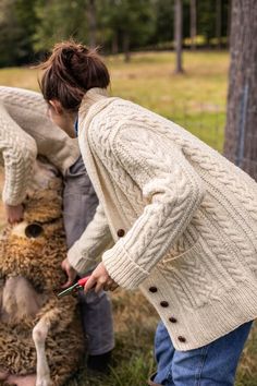 a woman in a white cardigan is petting a sheep that has been sheared