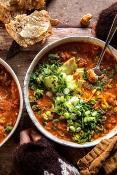 two bowls of soup with bread on the side and someone holding a spoon in their hand