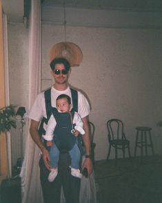 a man holding a baby in his arms wearing sunglasses and a hat on top of his head